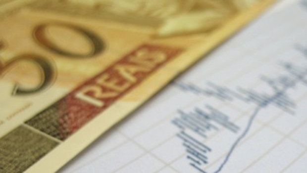 Stock market charts for investor analysis, with Brazilian Real $50 bills and pen, using selective focus on graph and pen.